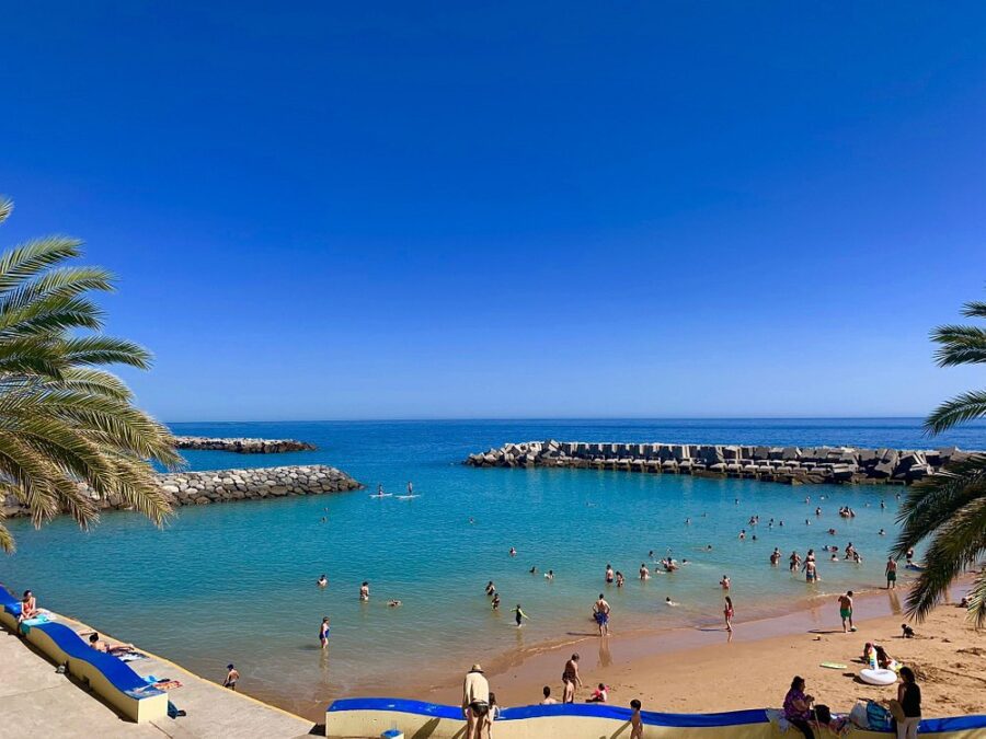 Praia da Calheta, Madeira Island, featuring a vibrant beach scene with swimmers and sunbathers enjoying the warm sun