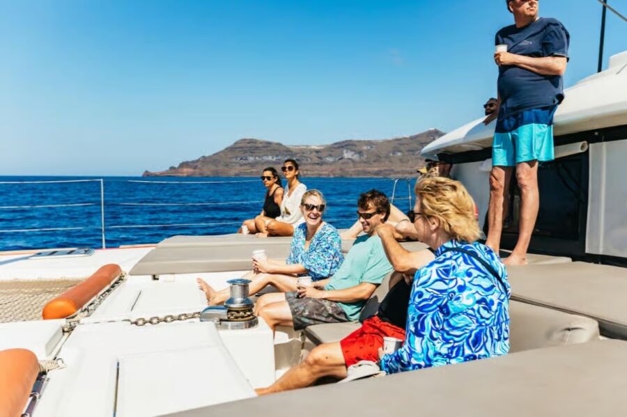 People relax on a catamaran deck, enjoying the ocean view during a premium sailing experience from Santorini.