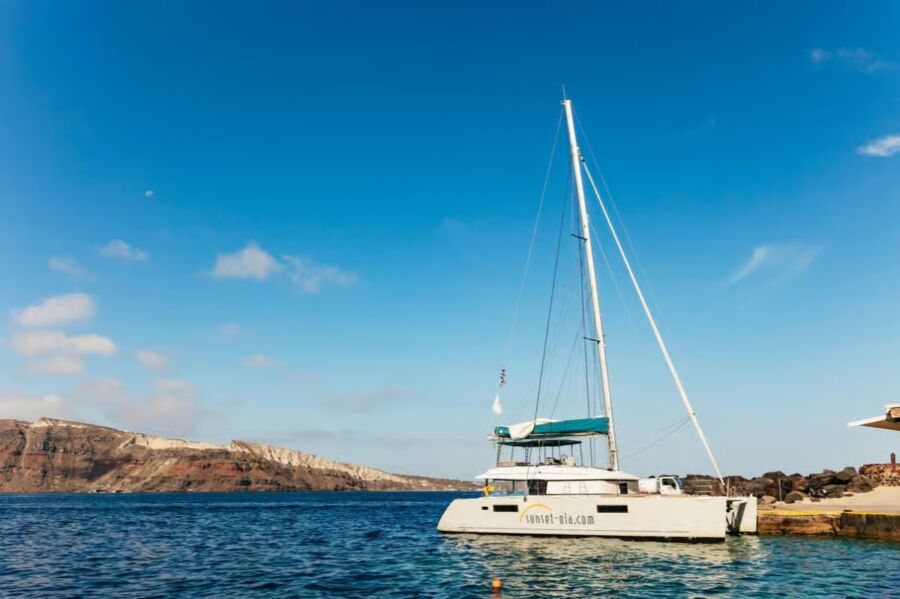 Catamaran rests in the water, surrounded by mountains, highlighting a premium sailing experience from Santorini.