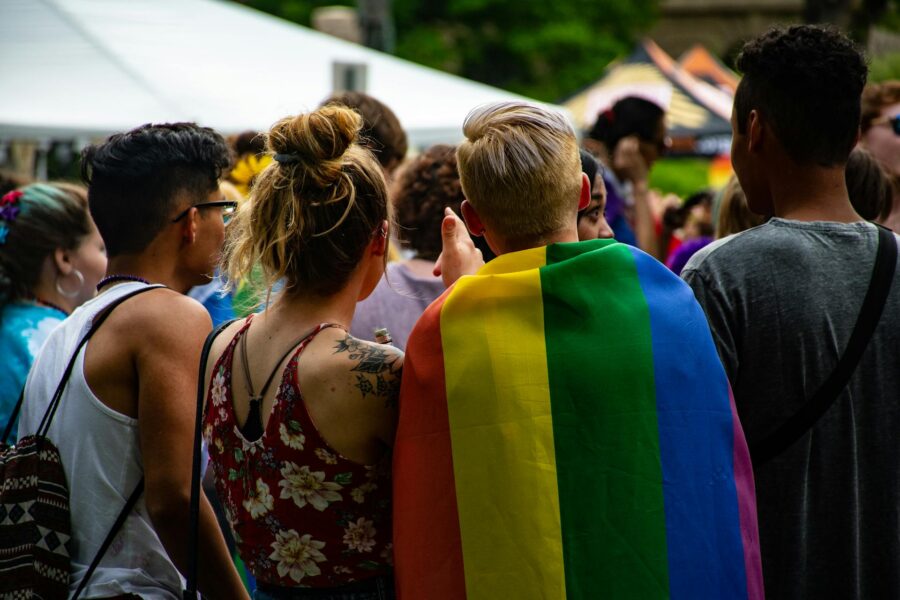 LGBTQ+ pride celebration with rainbow flag and diverse attendees in a lively park setting.