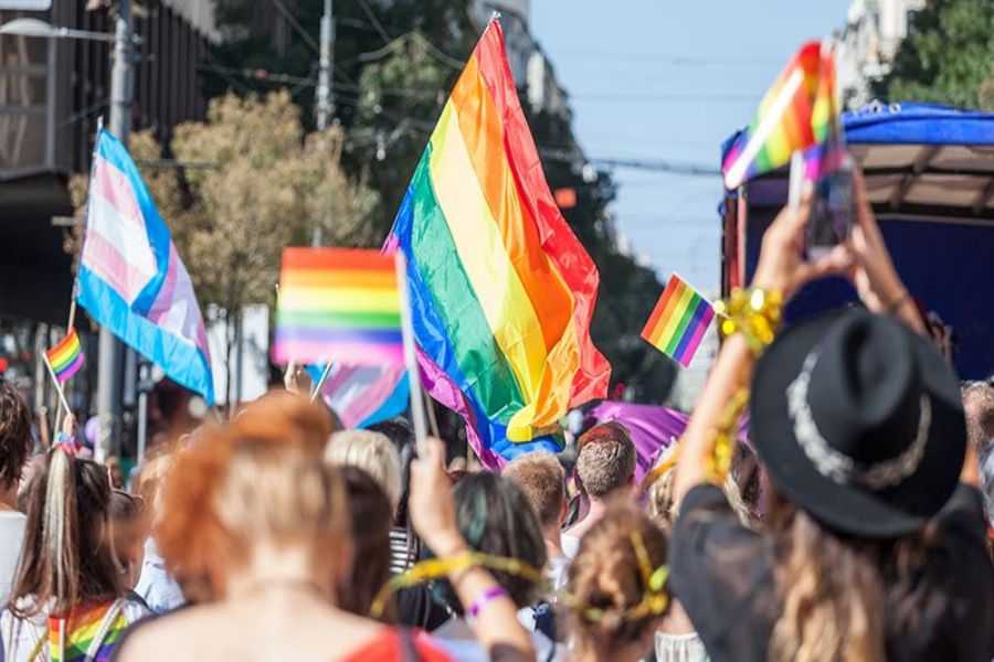 LGBTQ+ pride parade with colorful flags, joyful participants, and urban backdrop.