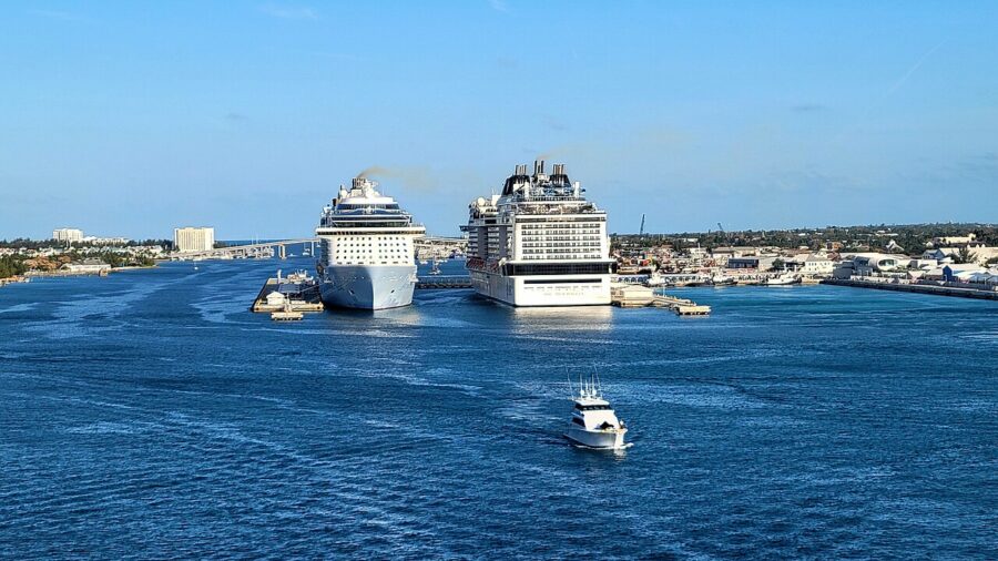 Two large cruise ships docked at Prince George Wharf Nassau bustling harbor, a small boat in the foreground, under a clear blue sky. The scene is serene and vibrant.