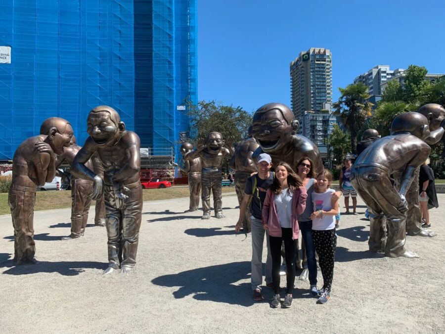 Three people pose in front of statues during a private walking tour in Vancouver.
