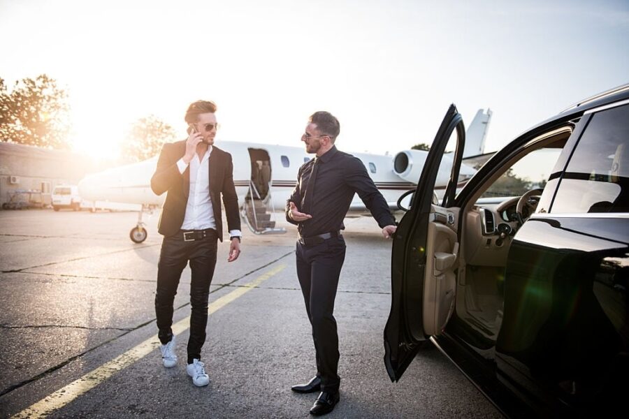 Businessmen boarding private jet beside luxury SUV for Crete airport transfer.