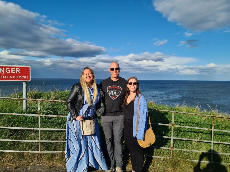 Three people smiling by a railing, with the ocean and blue sky behind on a Private St. Andrews Town Guided Walking Tour