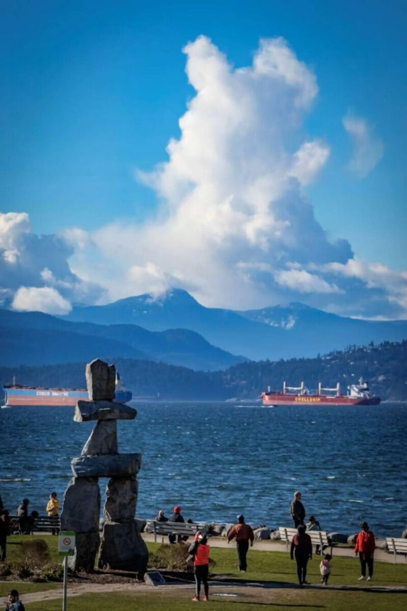 People stroll along the Vancouver shore with a prominent statue visible in the background during a private walking tour.
