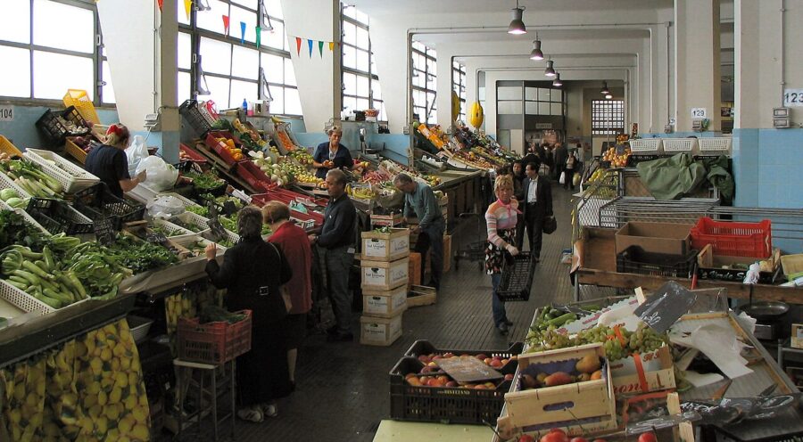 Trieste covered market aisle with fresh fruits and vegetables on bustling stalls.
