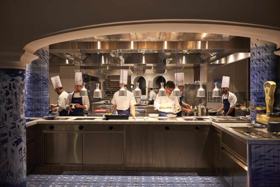 Modern kitchen with chefs cooking, high-end appliances, blue tiles, and elegant lighting.