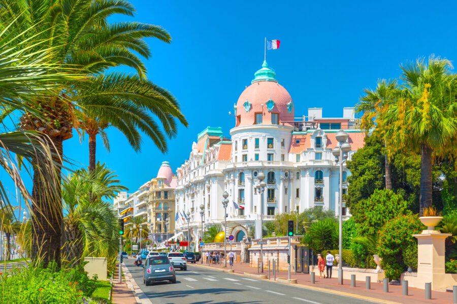 Scenic view of Promenade des Anglais in Nice, France, featuring a road lined with cars and palm trees along the coastline