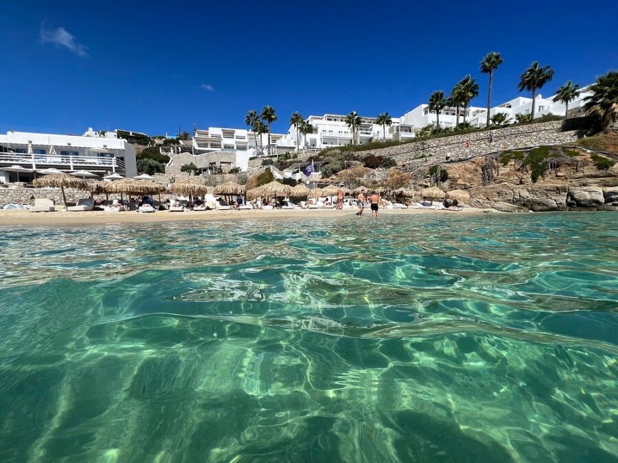 Serene Psarou Beach in Greece, with crystal-clear water and vibrant palm trees lining the shore.

