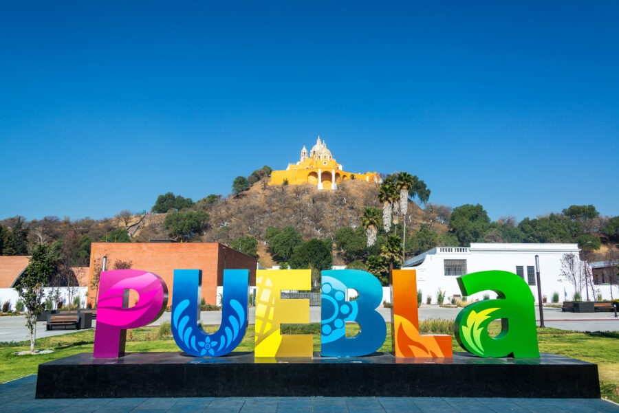 Close-up of the Puebla sign in Cholula, Mexico, with colorful letters against a green landscape