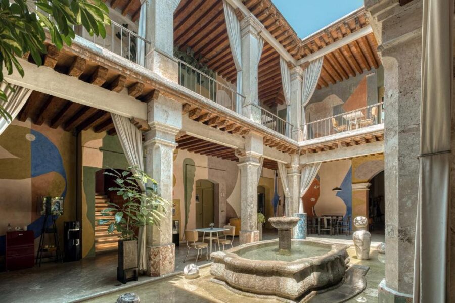 The courtyard of Pug Seal Oaxaca showcases a decorative fountain and an artistic mural on the wall in Oaxaca City, Mexico.
