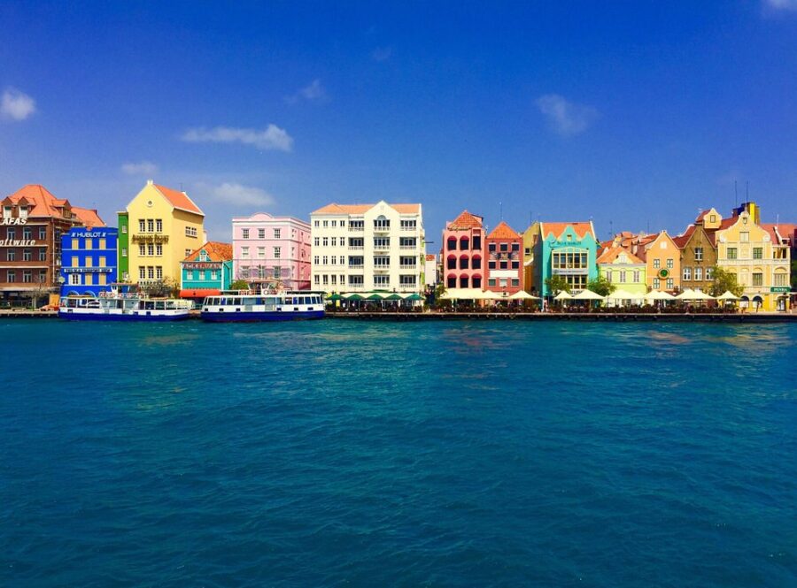 Colorful houses line the waterfront in Punda, Curacao, showcasing vibrant architecture against a city backdrop.
