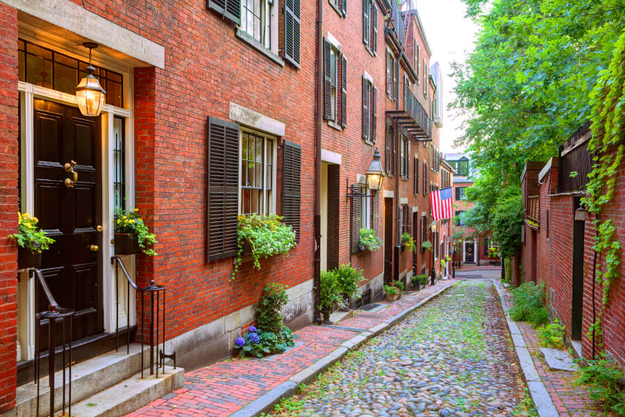 Historic American street scene with red brick buildings, cobblestone path, greenery, and flag.