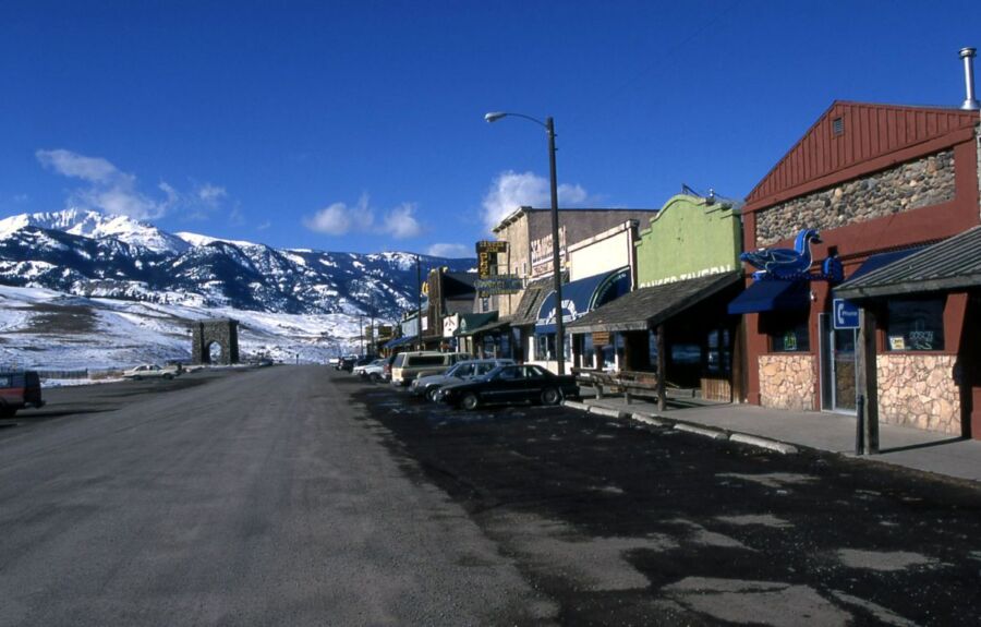 Charming small-town street with mountain backdrop, rustic shops, and parked cars under blue skies.