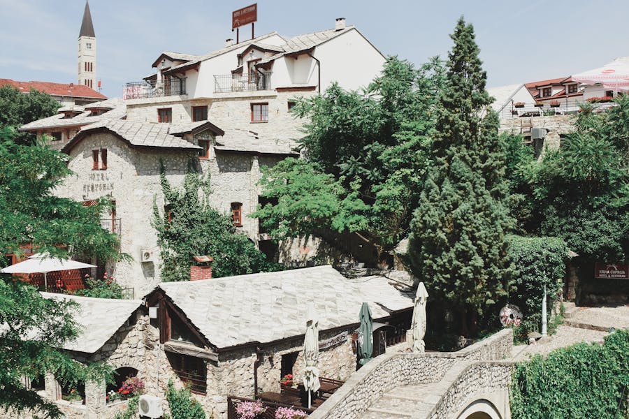 Quaint village with stone architecture, lush greenery, and a prominent tower against blue sky.