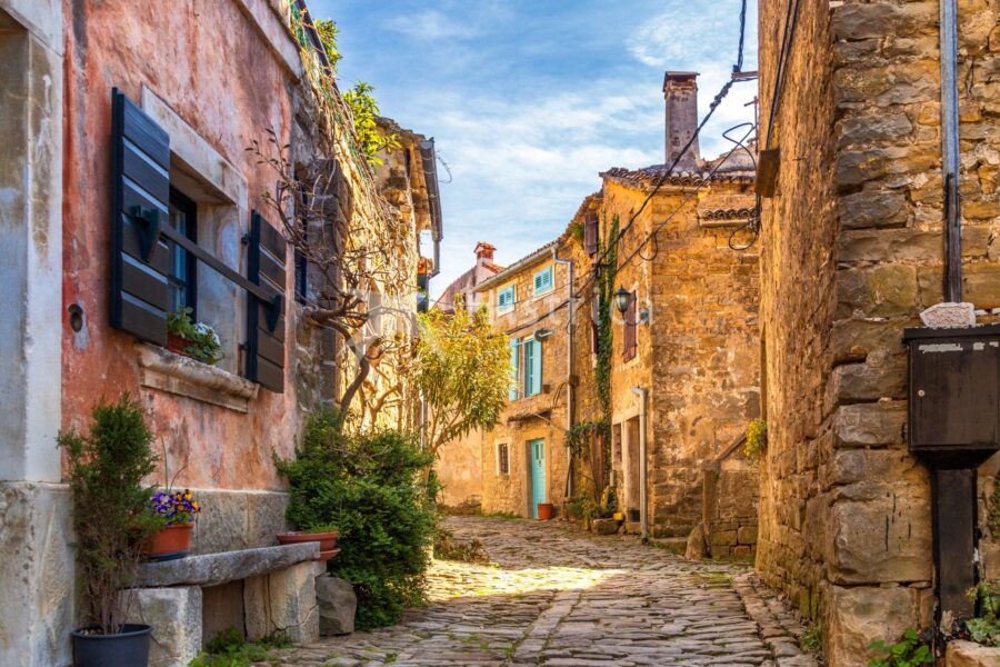 Quaint old town street with cobblestones, stone buildings, colorful shutters, and vibrant flowers.