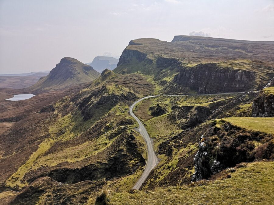 Scenic view of the winding road leading to Quiraing on the Isle of Skye, surrounded by lush green hills and dramatic cliffs.
