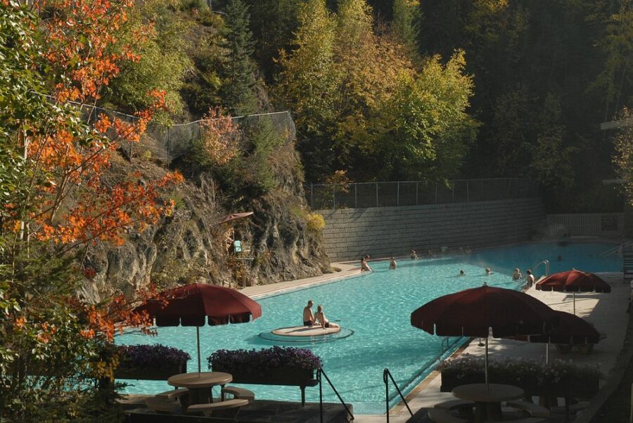 Radium Hot Springs features a pool encircled by trees, with visitors relaxing and enjoying the natural surroundings.
