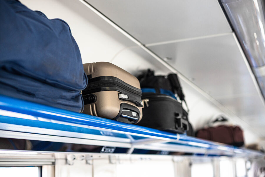 Luggage compartment of a railway train, showcasing overhead storage and seating area for passengers.