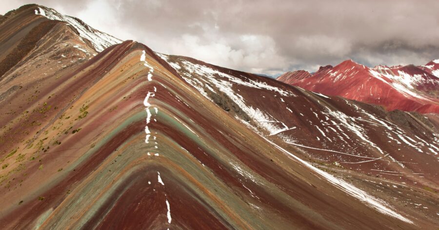 Colorful striped mountain ridges with dramatic topography under cloudy sky.