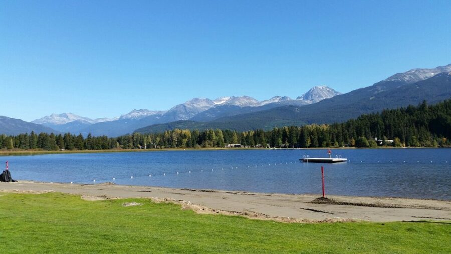 Picturesque lake with mountains in the background and a vibrant green field at Rainbow Park, Whistler, Canada.