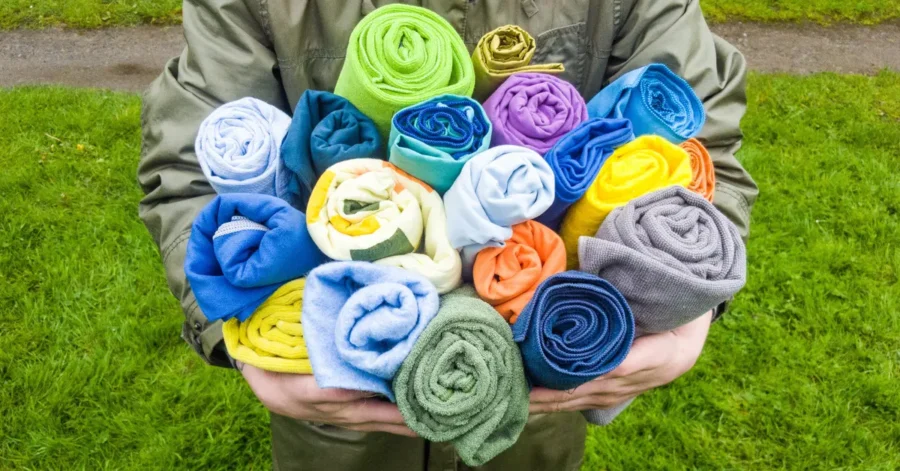 Vibrant rolled microfiber towels in various colors held outdoors on a green lawn.