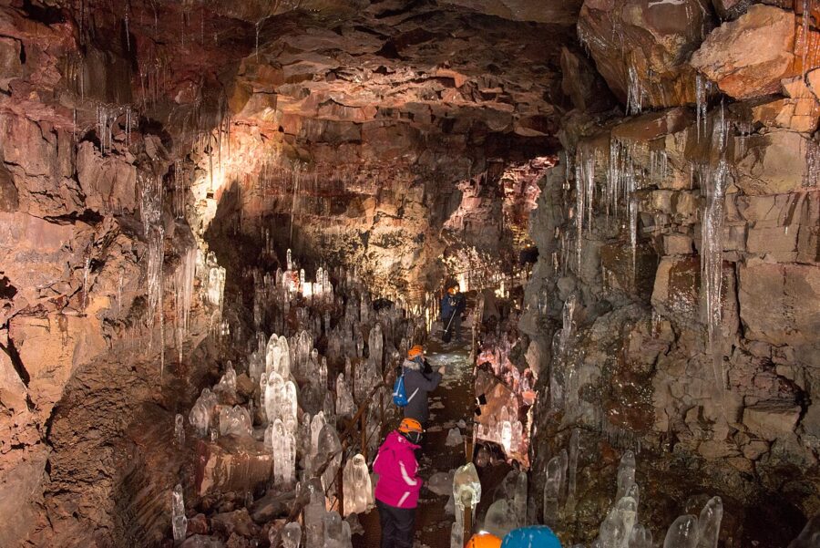 People walk through Raufarhólshellir cave in Iceland, surrounded by stunning ice formations.