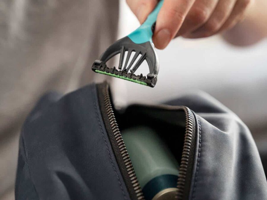 Close-up of a modern razor in hand with a travel bag in the background.