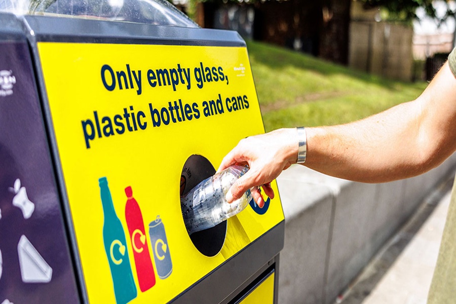 Yellow recycling bin for bottles, containers, and cans in outdoor park setting.