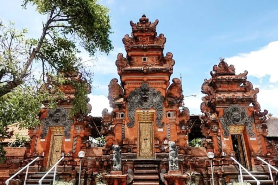 Balinese red brick temple facade with ornate golden doors, stone guardians, and traditional split gates.