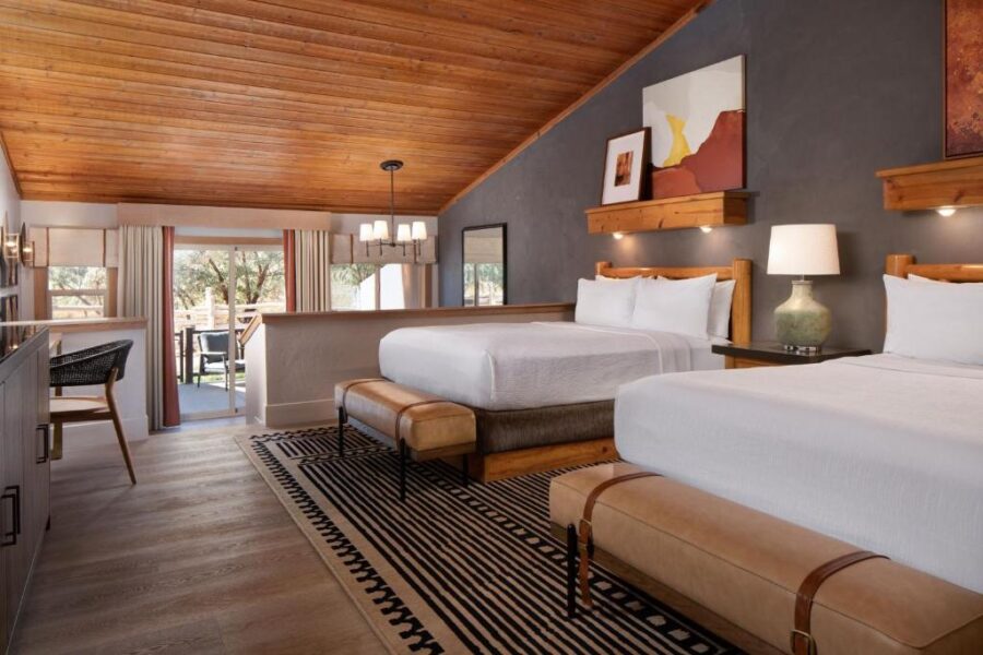 Two beds in a cozy room with wooden ceilings and a fireplace at Red Cliffs Lodge in Moab.