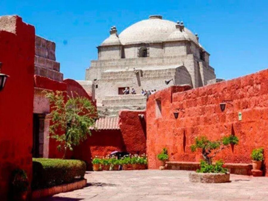 Sunlit red courtyard of Santa Catalina Monastery with stone domes, colonial architecture, and plants.