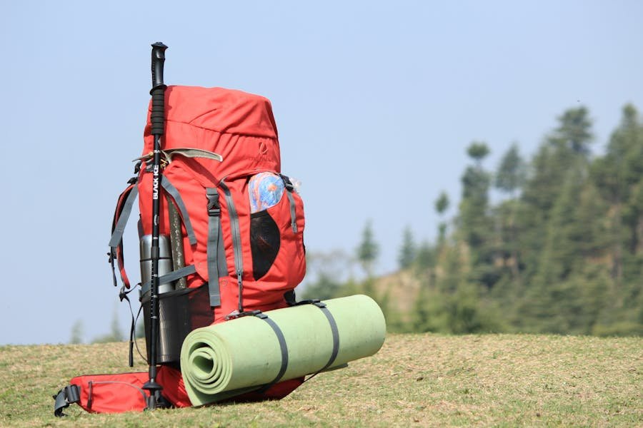 Red hiking backpack with camping gear, sleeping pad, and trekking poles on grassy hill.