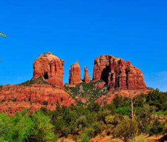 Red sandstone formations with greenery under a clear blue sky in a serene landscape.