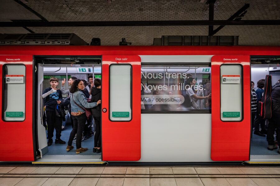 Barcelona red metro train with commuters boarding on busy platform.