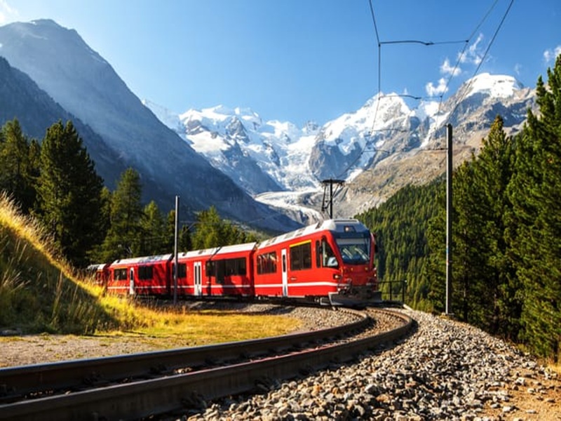 Red train in mountainous landscape, scenic railway journey, vibrant nature, adventure, travel scene.