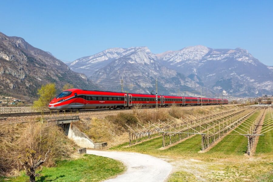 Red train crossing vineyard with mountain backdrop. Scenic travel routes and modern rail technology.