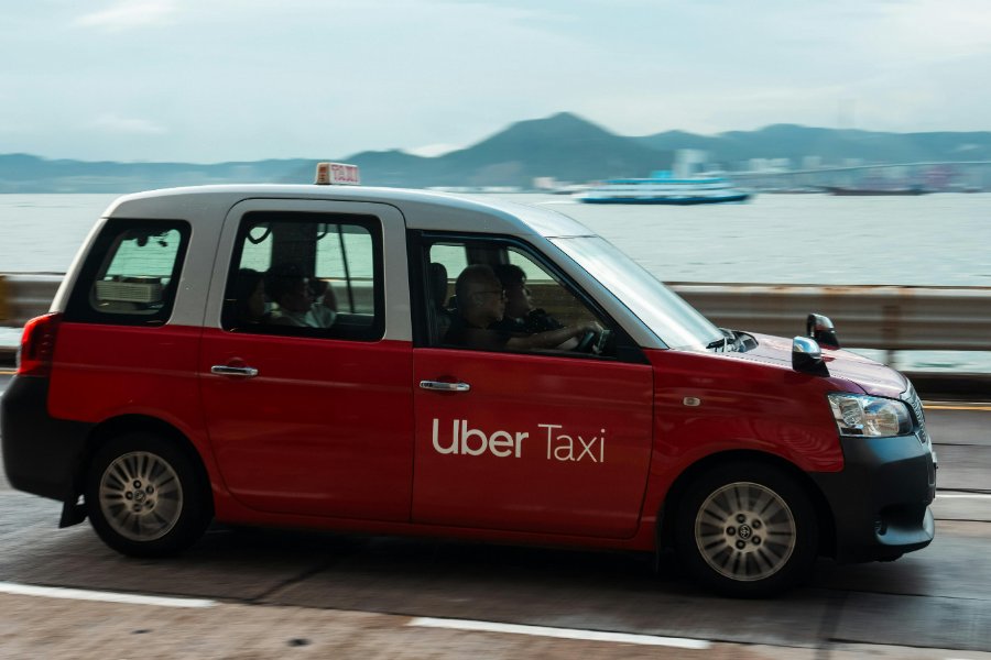 Red-and-white Uber taxi driving along Naxos coastal road by the sea.