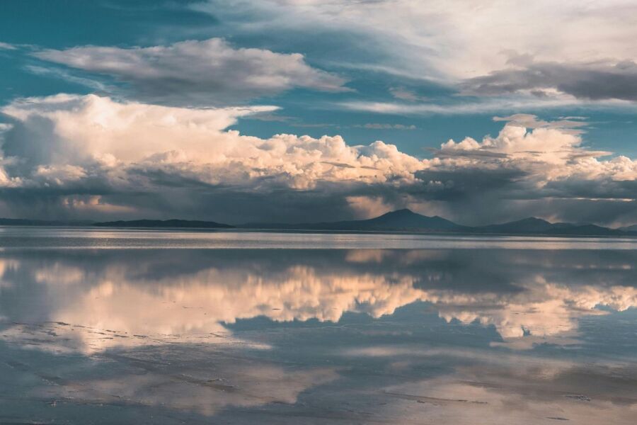 Serene mirrored lake landscape with dramatic clouds and distant mountains reflecting natures tranquility.
