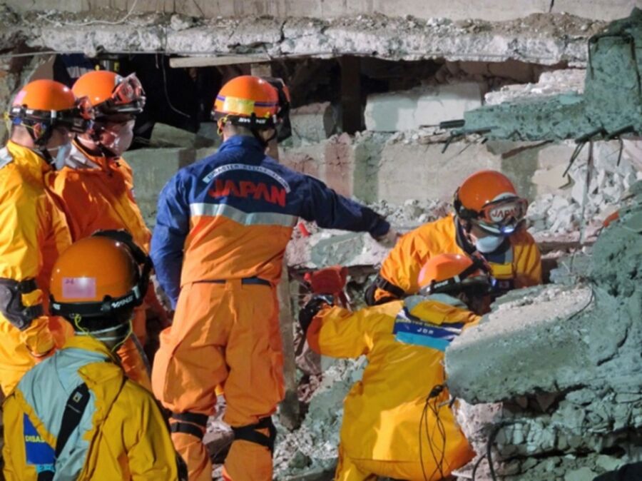 Rescue workers in orange uniforms conduct urgent search amidst building collapse debris.