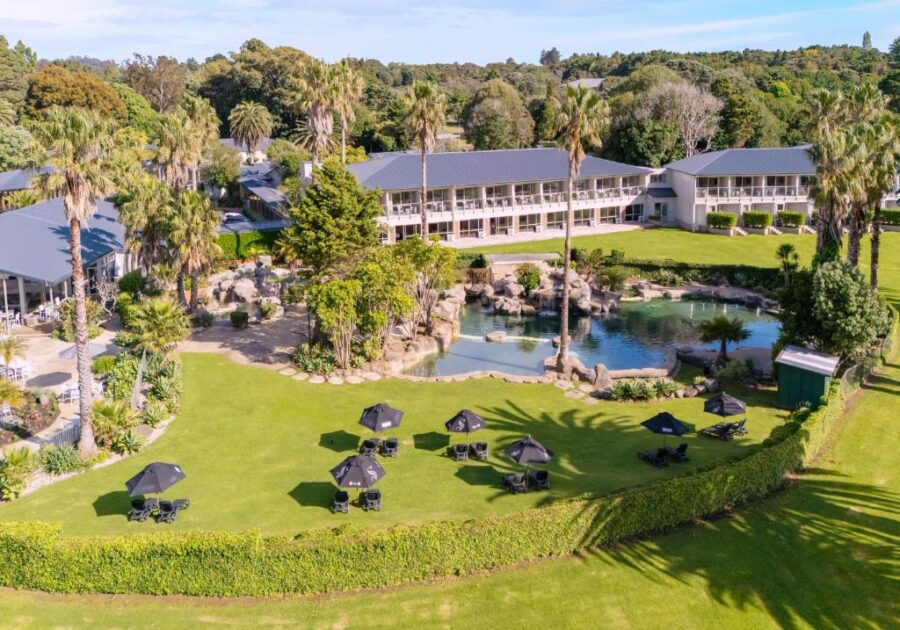 Aerial view of Copthorne Bay of Islands resort with lagoon pool, palm trees, and green lawns.