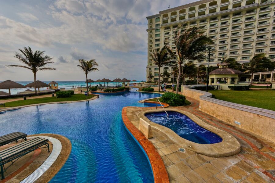 Luxurious resort scene with an infinity pool, ocean view, and modern hotel building.