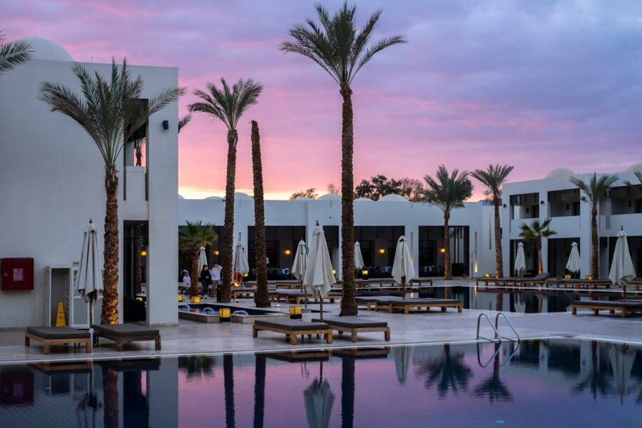 Luxury resort pool at sunset with palm trees, lounge chairs, and colorful twilight sky.