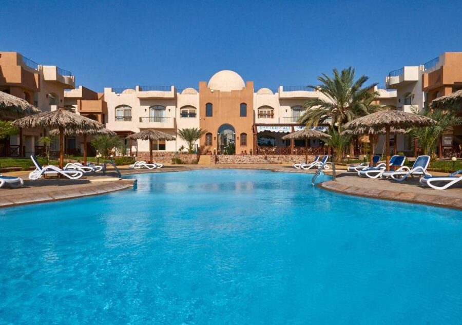 Luxury desert resort hotel with large swimming pool, sun loungers, palm trees and clear blue sky.