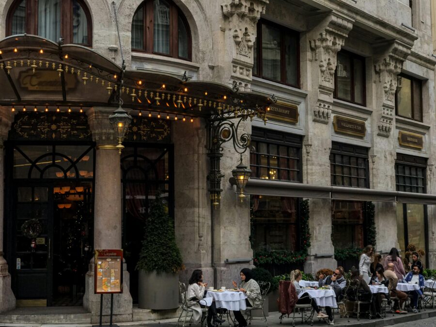Historic stone restaurant facade with canopy and outdoor sidewalk cafe seating and warm lighting.