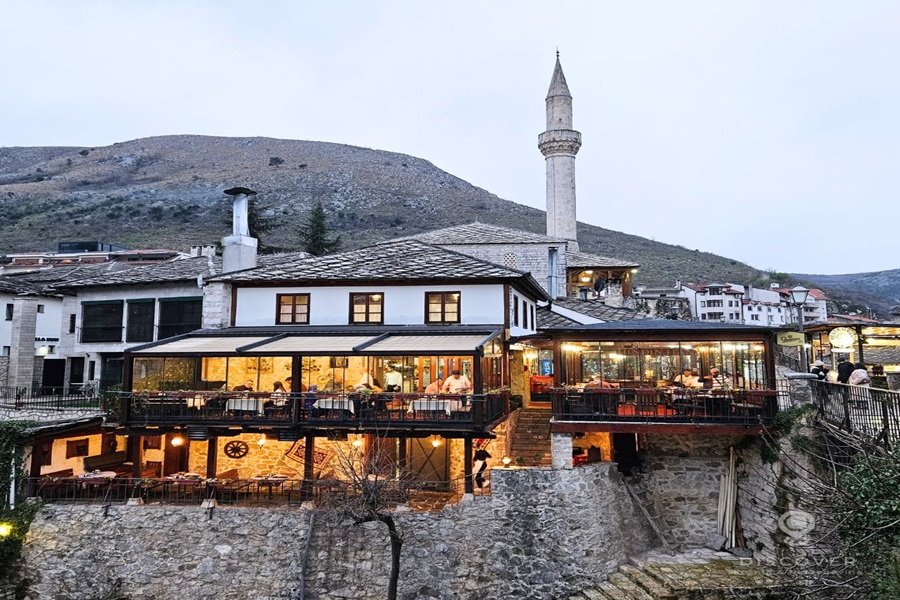 Cozy restaurant with mountain view, modern-traditional design, near mosque at twilight.