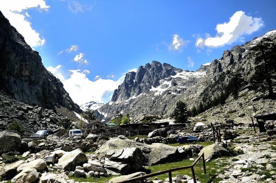 Scenic view of Restonica Valley featuring rocky terrain and lush trees amidst a mountainous backdrop.