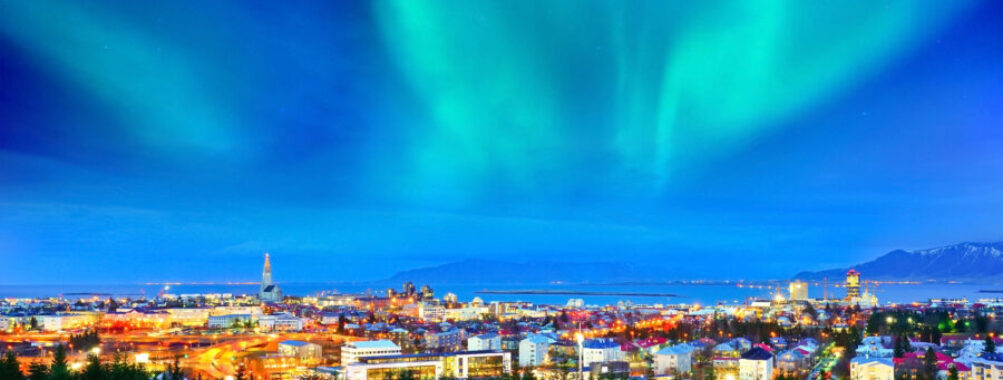 Northern lights illuminate the sky above Reykjavik's city center, showcasing vibrant colors against a dark backdrop.