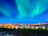 Northern lights illuminate the sky above Reykjavik's city center, showcasing vibrant colors against a dark backdrop.